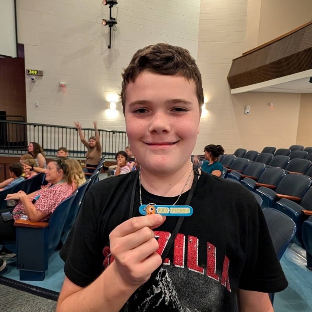A student smiles with his citizenship award in the auditorium.
