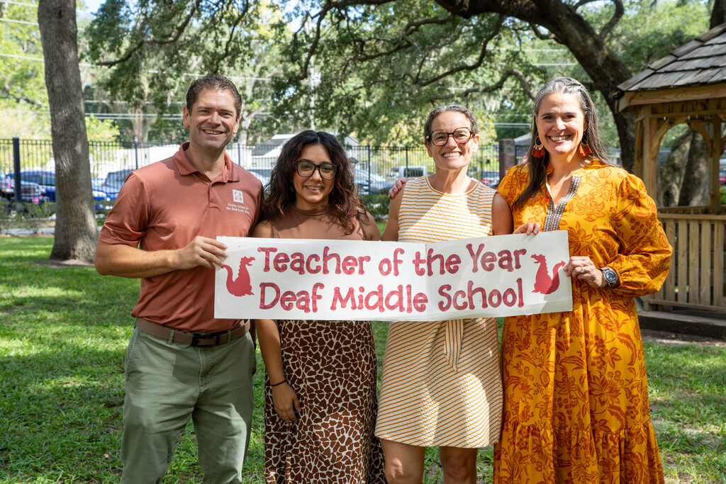 Alicia smiles with administration and a sign that says "Teacher of the Year, Deaf Middle School"
