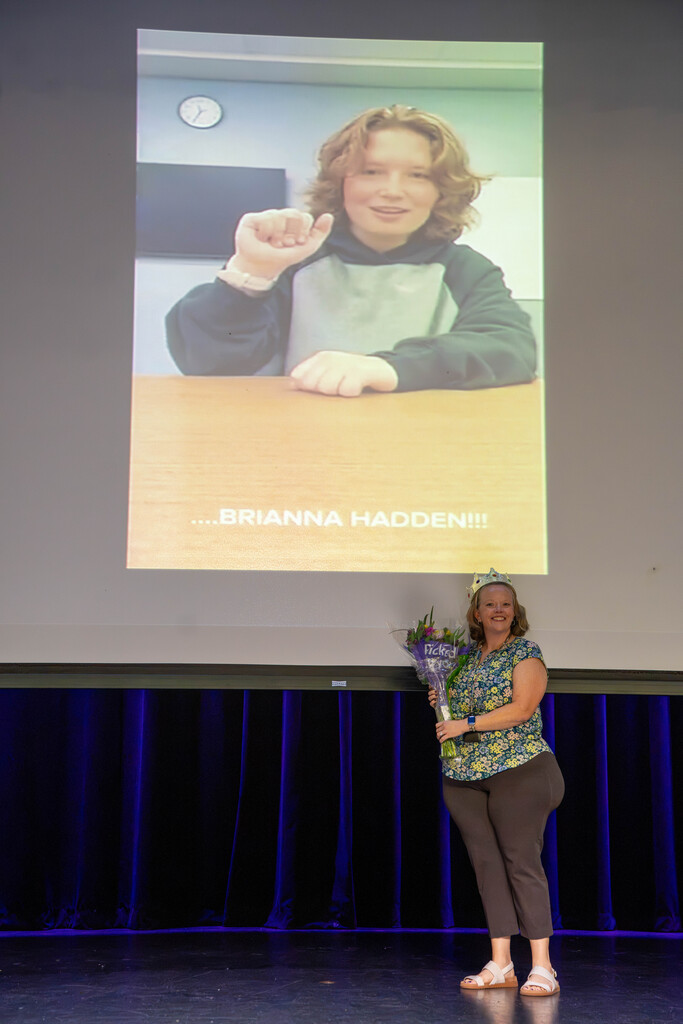 Brianna smiles with former student on the screen on stage.