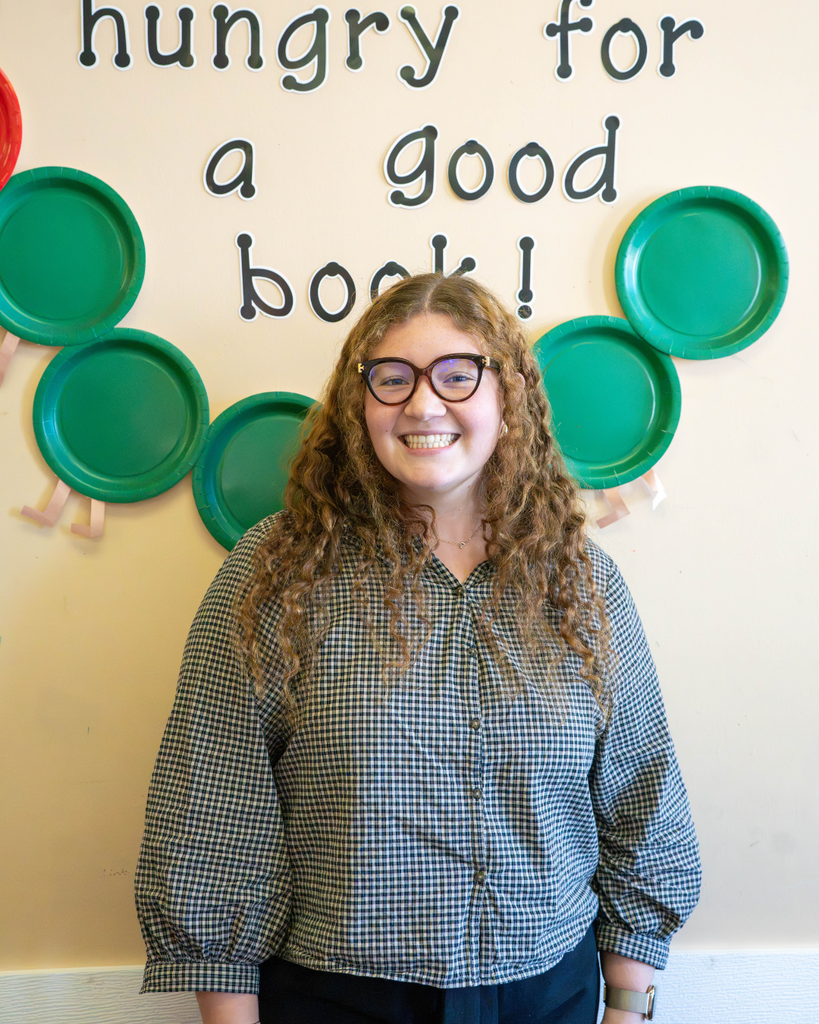 Deaf High School rookie finalist (Alexis Griffin) stands in front of a classroom display featuring the words “hungry for a good book!” and several decorative green plates.