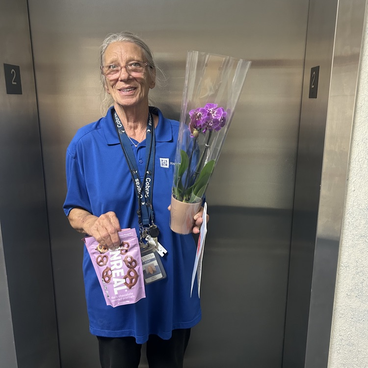 Ms. Faye holding flowers and a bag of chocolate covered pretzels 
