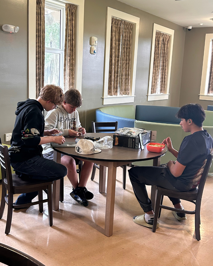 Three students sit at a table and work on legos together.