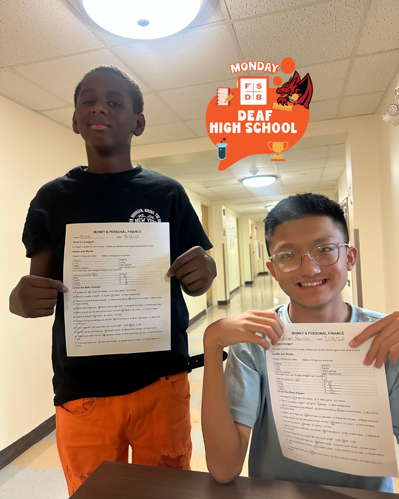 Two students holds a "money and personal finance" practice paper smiles for their photo.