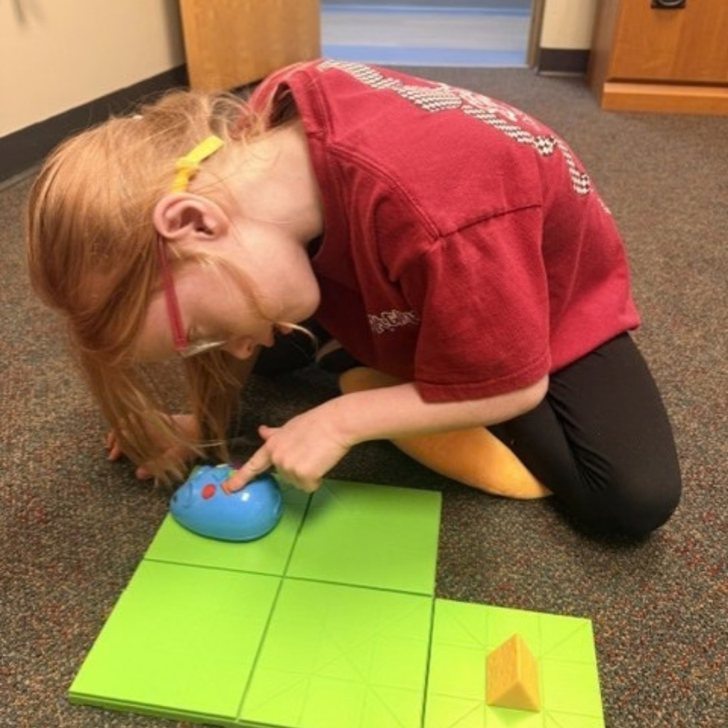 A student kneels on the floor pressing buttons on the blue mouse inside the O&M classroom. 