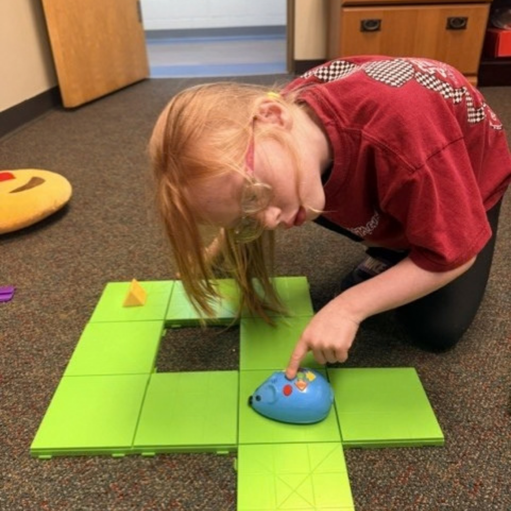 A student built a longer track maze and she bends over to press on the buttons inside the O&M classroom. 