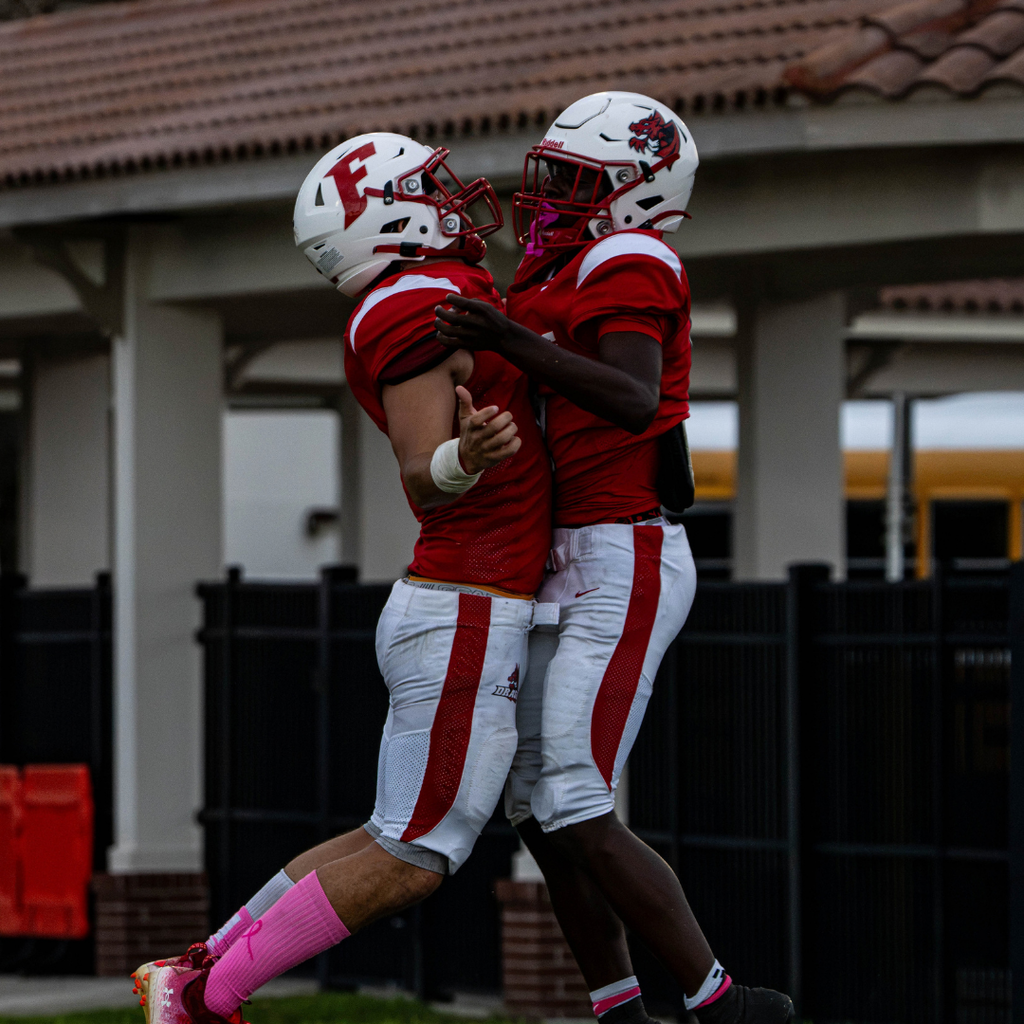 Two FSDB football players jump and chest bump each other. 