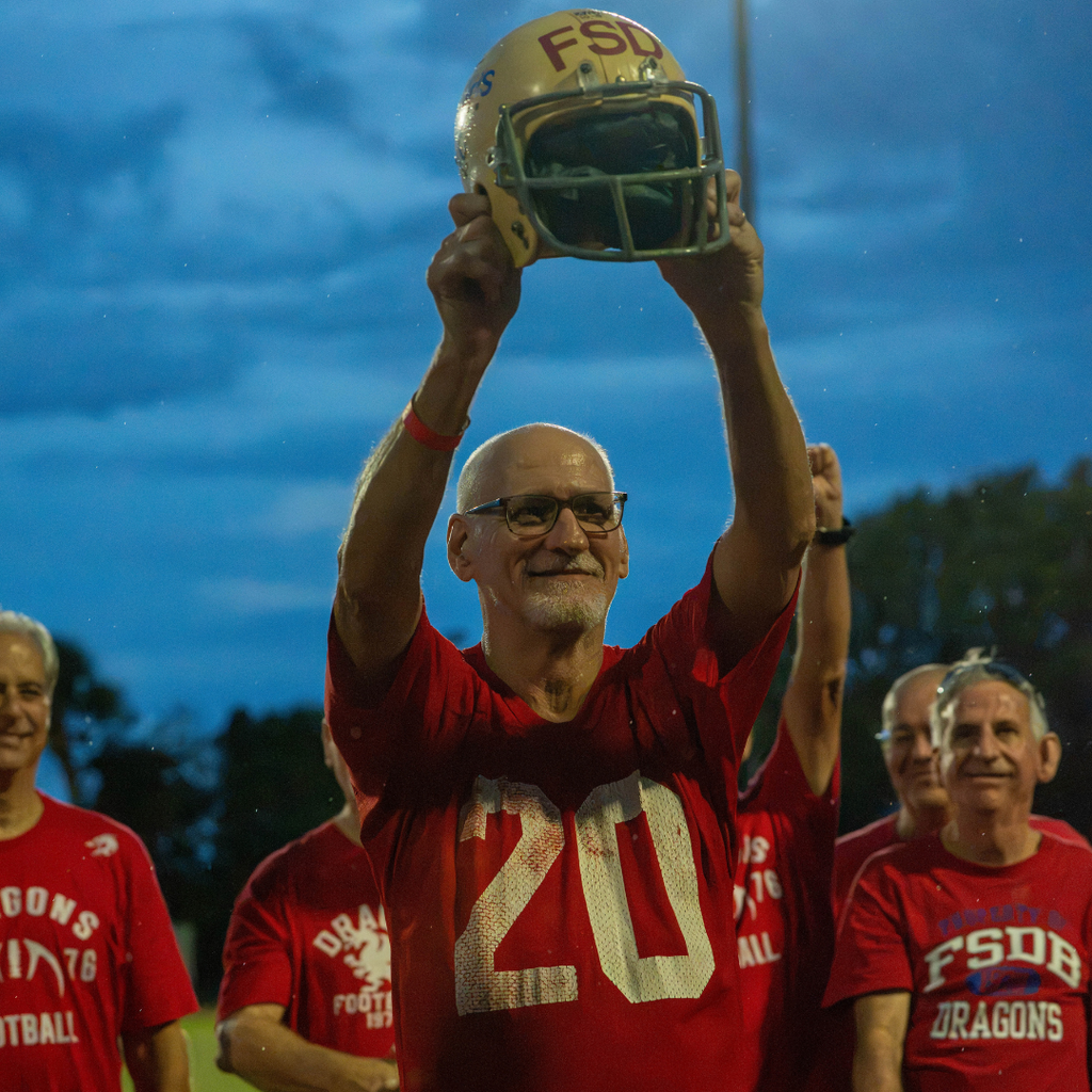 A alumni football player holds the helmet proudly on the field. 