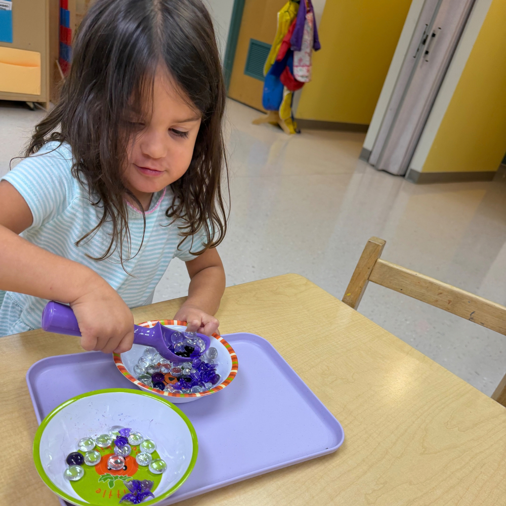 ELC student scoops halloween marbles from one bowl to another. 