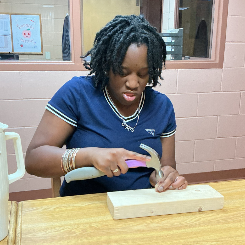 Close up of a student hammering a screw into wood.