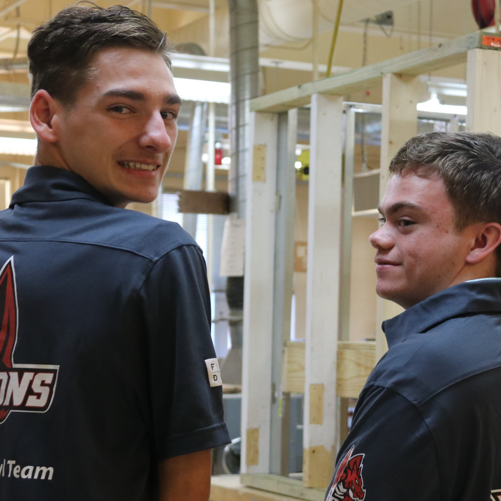Two students match and smile for a photo inside construction classroom. 