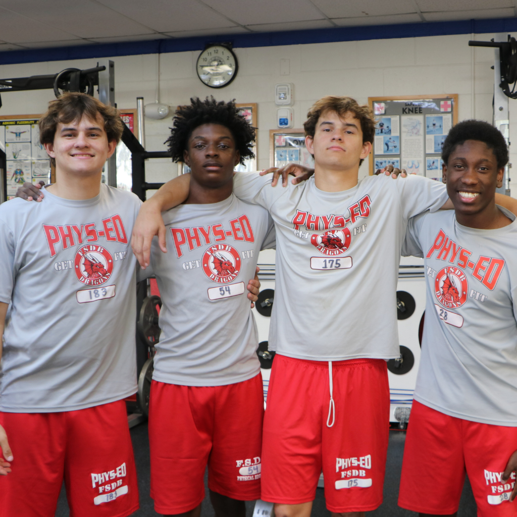 Four students matching in PE clothing inside the weightlifting room. 