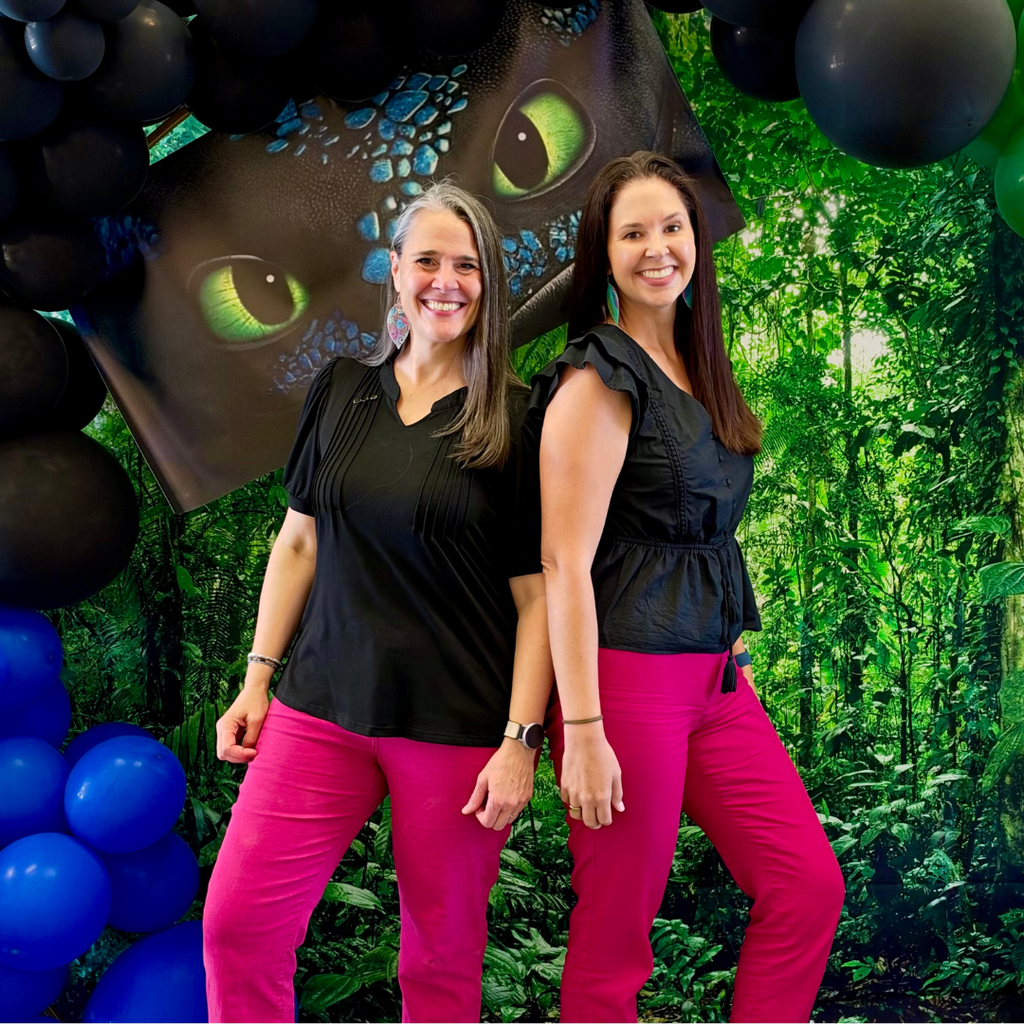 Two staff members match in pink pants and black shirts with a dragon background. 