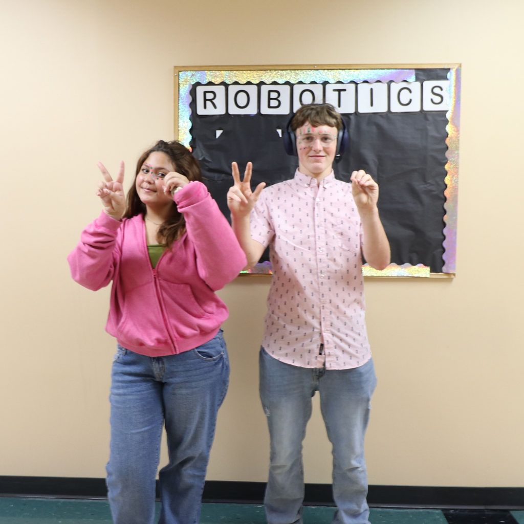 Two students dressed in pink and green, and sign "2030" with their hands.