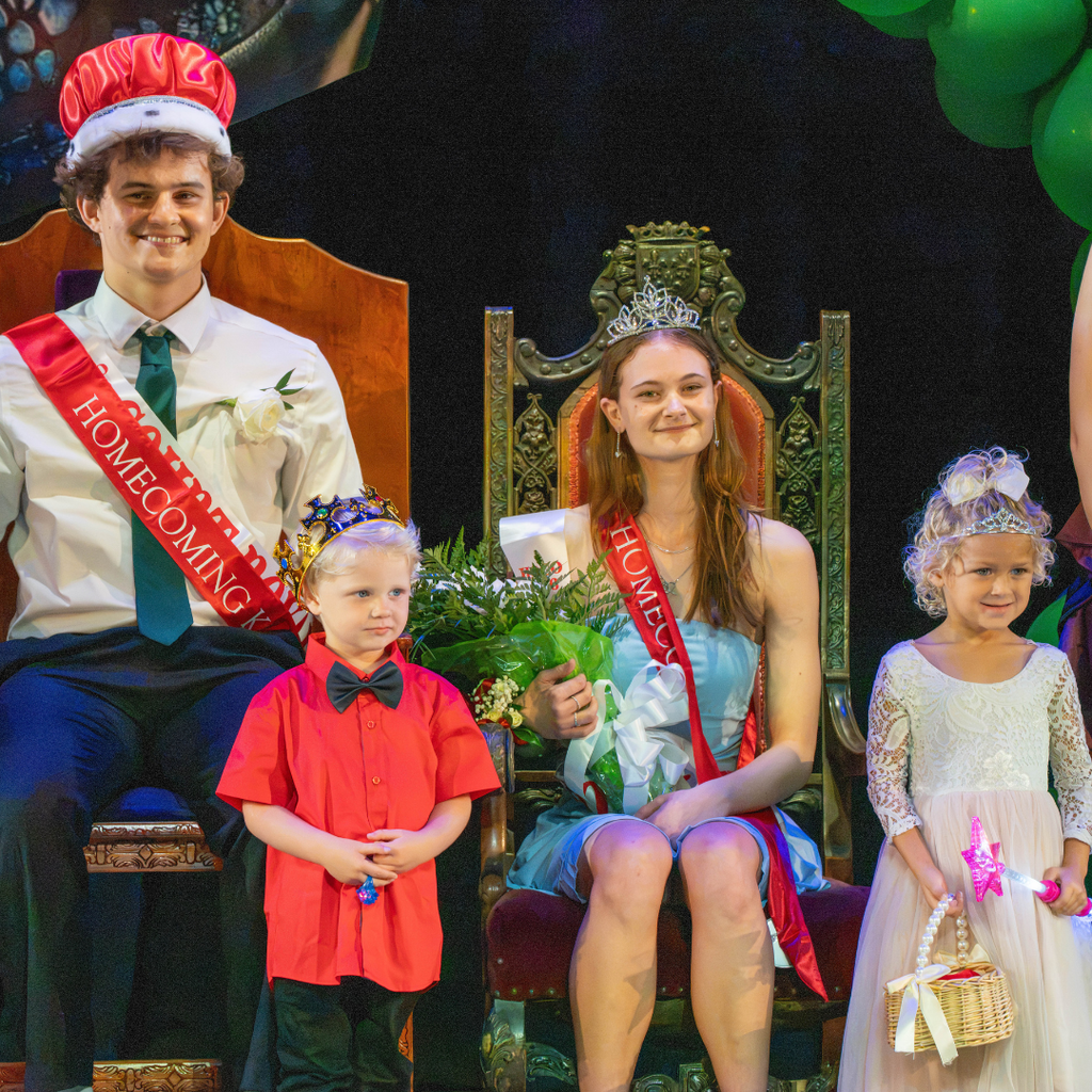 Homecoming King and Queen sit on the chairs and smile with two ELC students on stage in Kirk. 