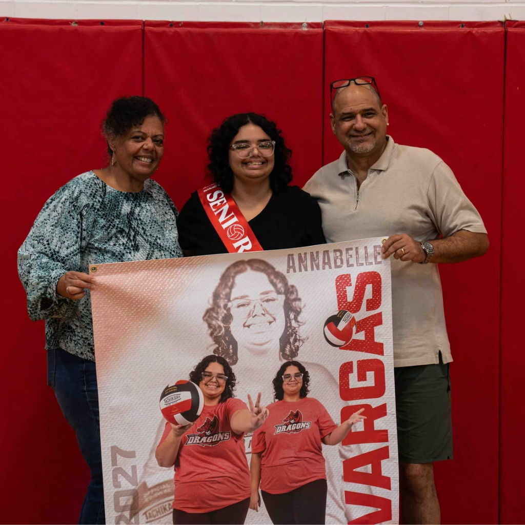 Senior smiles with her parents inside the gym.