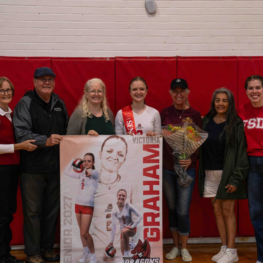 Senior smiles with her family and coach inside the gym.