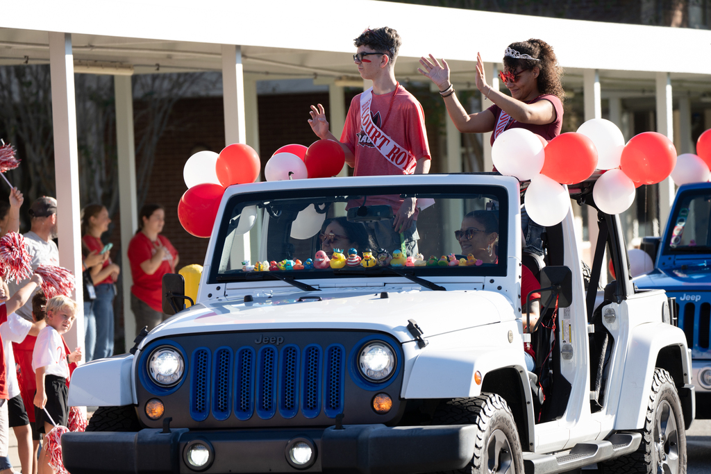 Royalty Court stands inside a Jeep decorated with red and white balloons. 