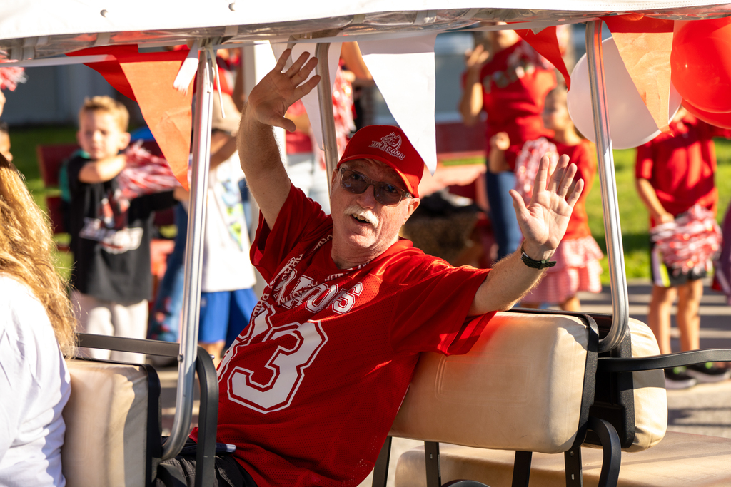 A staff member waves inside a golf cart. 