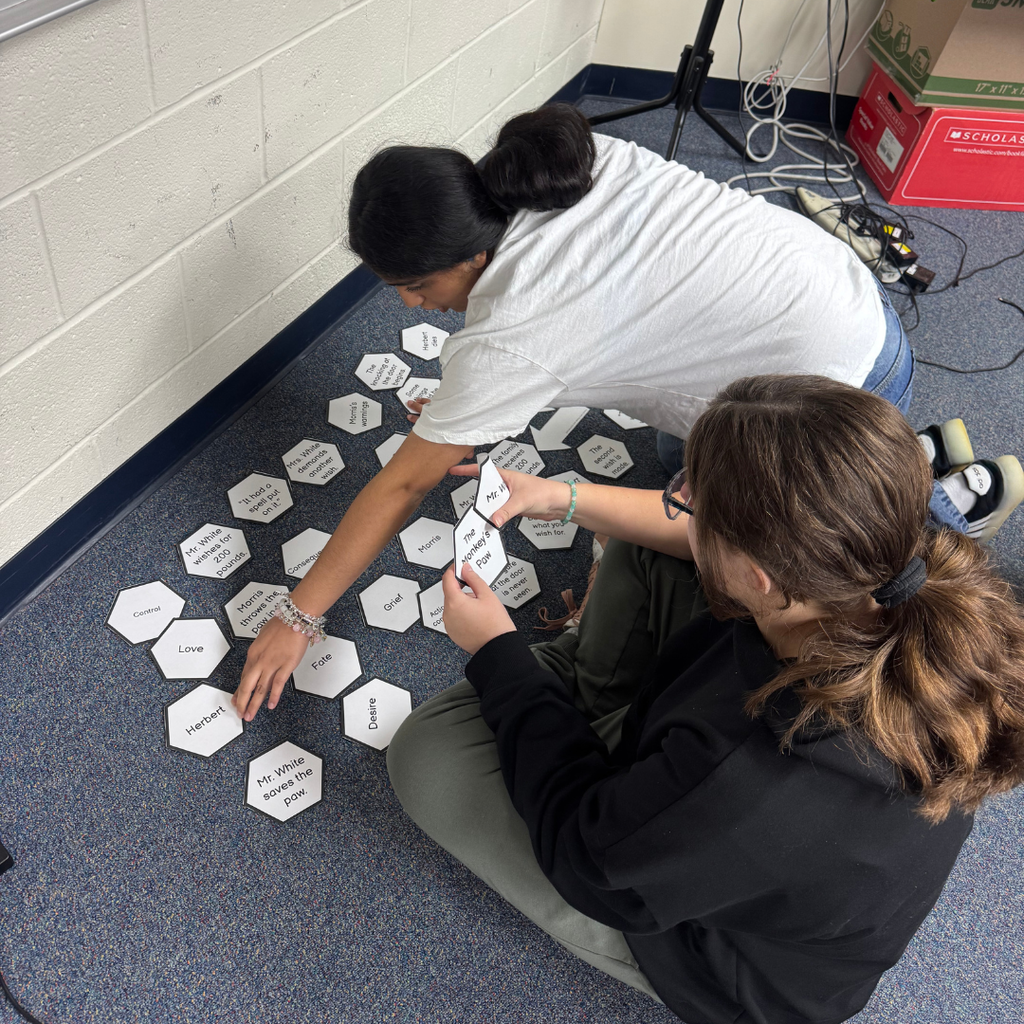 Two students sitting on the floor working together to match cards inside the classroom. 