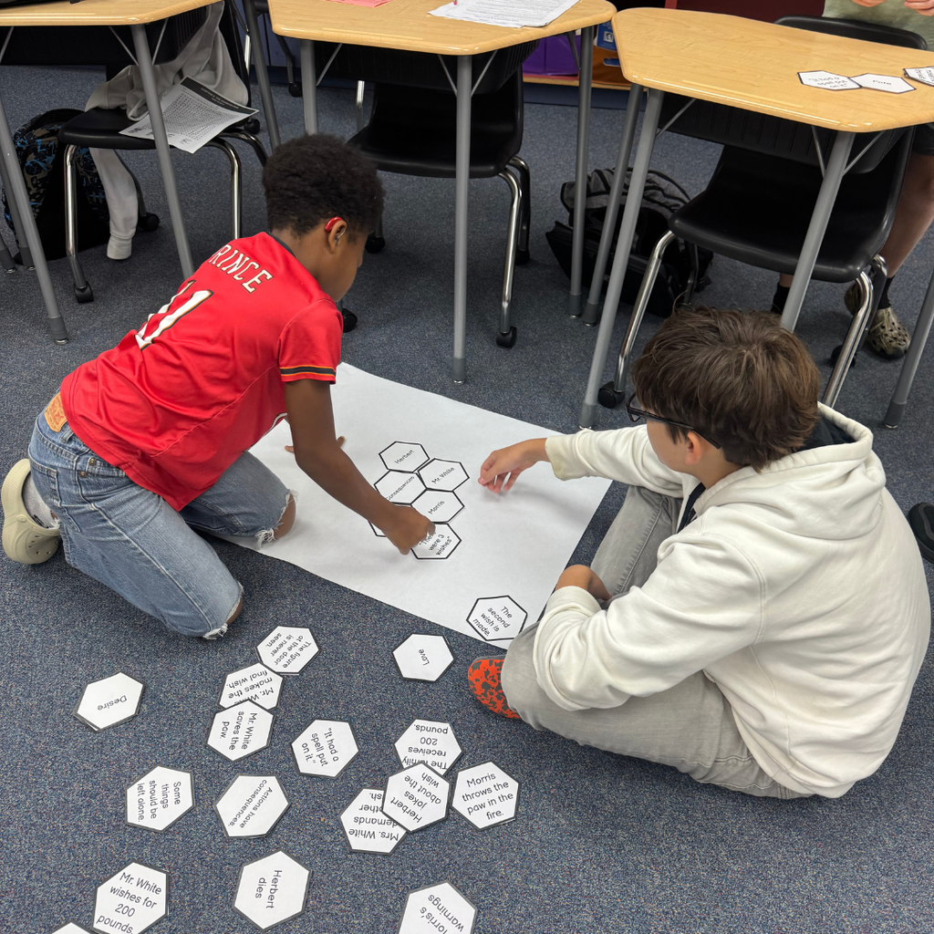 Two students work together to match cards on the floor. 