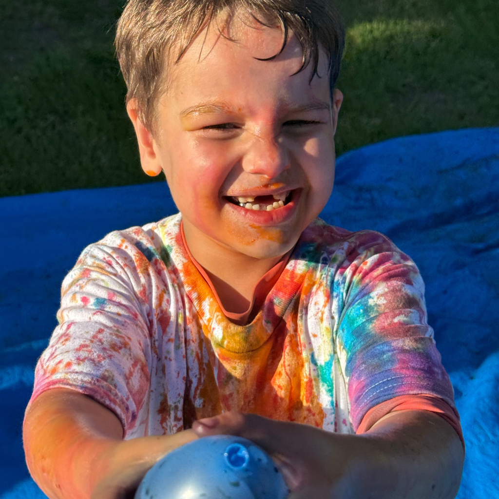 Student covered in washable dye smile for his photo holding a blue balloon. 