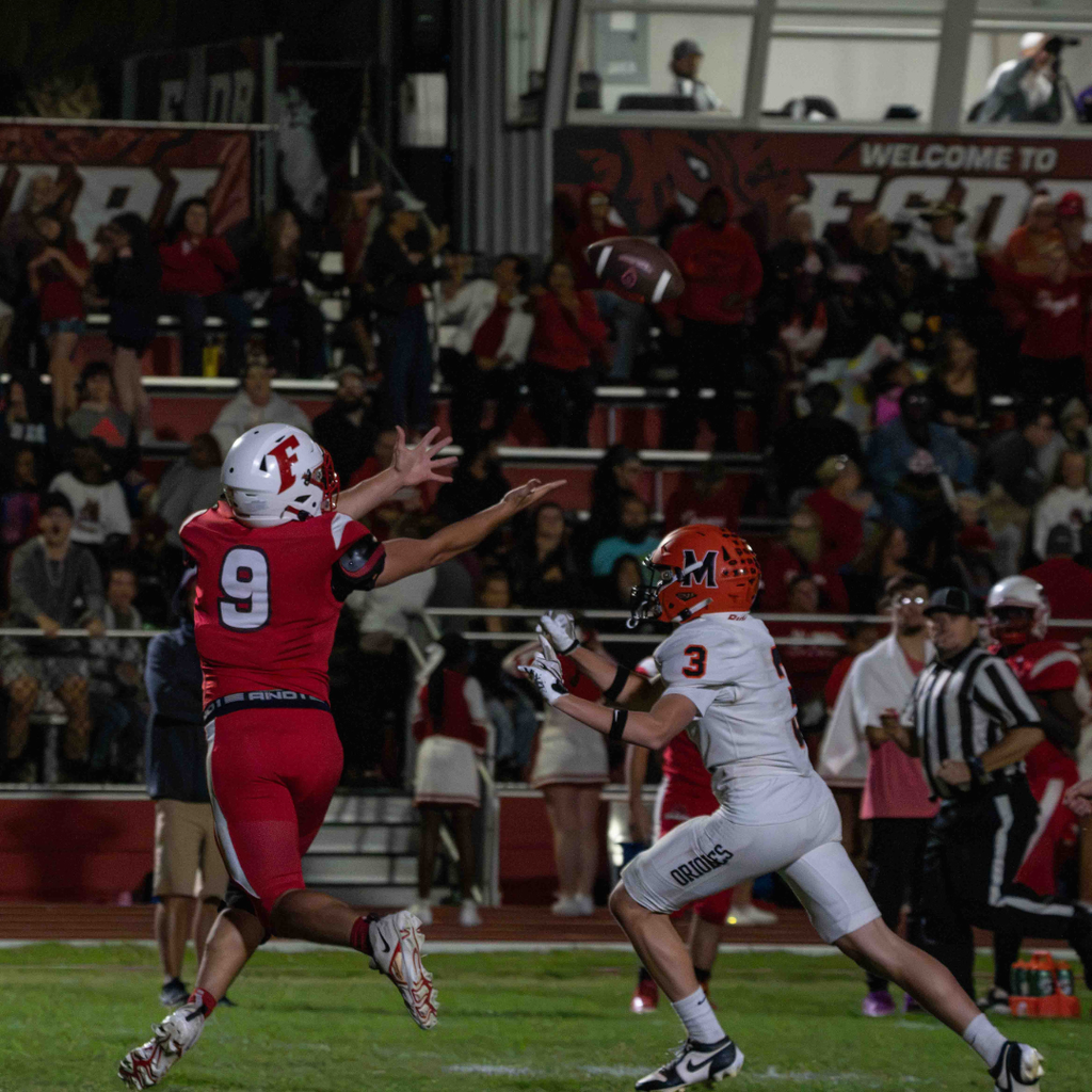 A FSDB football player holds his hands up ready to catch the ball, while the MSD player tries to stop him. 
