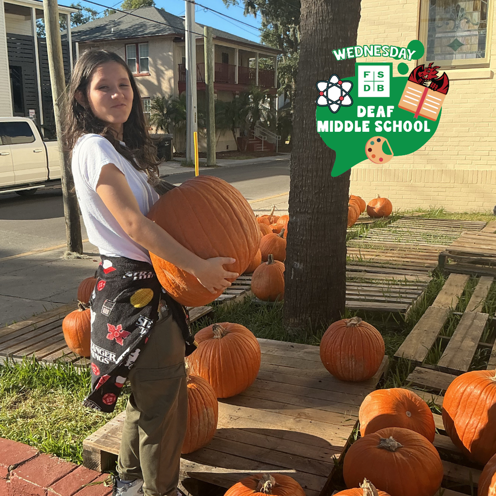 A student holds a big pumpkin and smiles for her photo. 