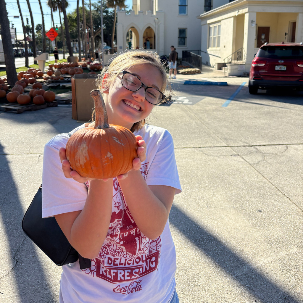 Student holds a tiny pumpkin and smiles for the camera. 
