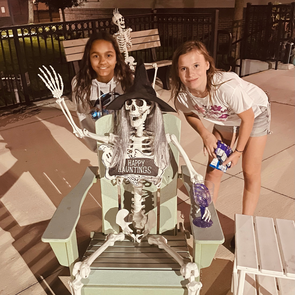 Two students smile with a Skelton sitting on a chair outside the dorm. 
