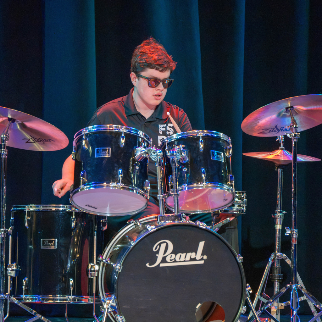 A student plays the drums for the audience on stage in Kirk.