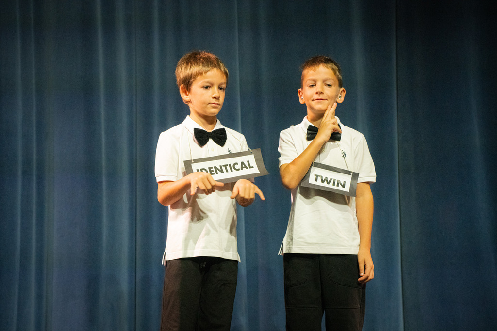 Twin boys wear white suit and black bow with the word 'Identical Twin" over their necks.