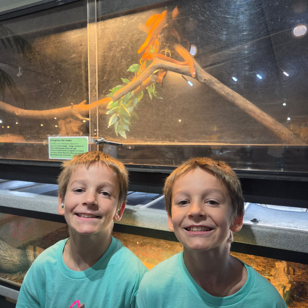 Two students smile with a snake inside a tank.