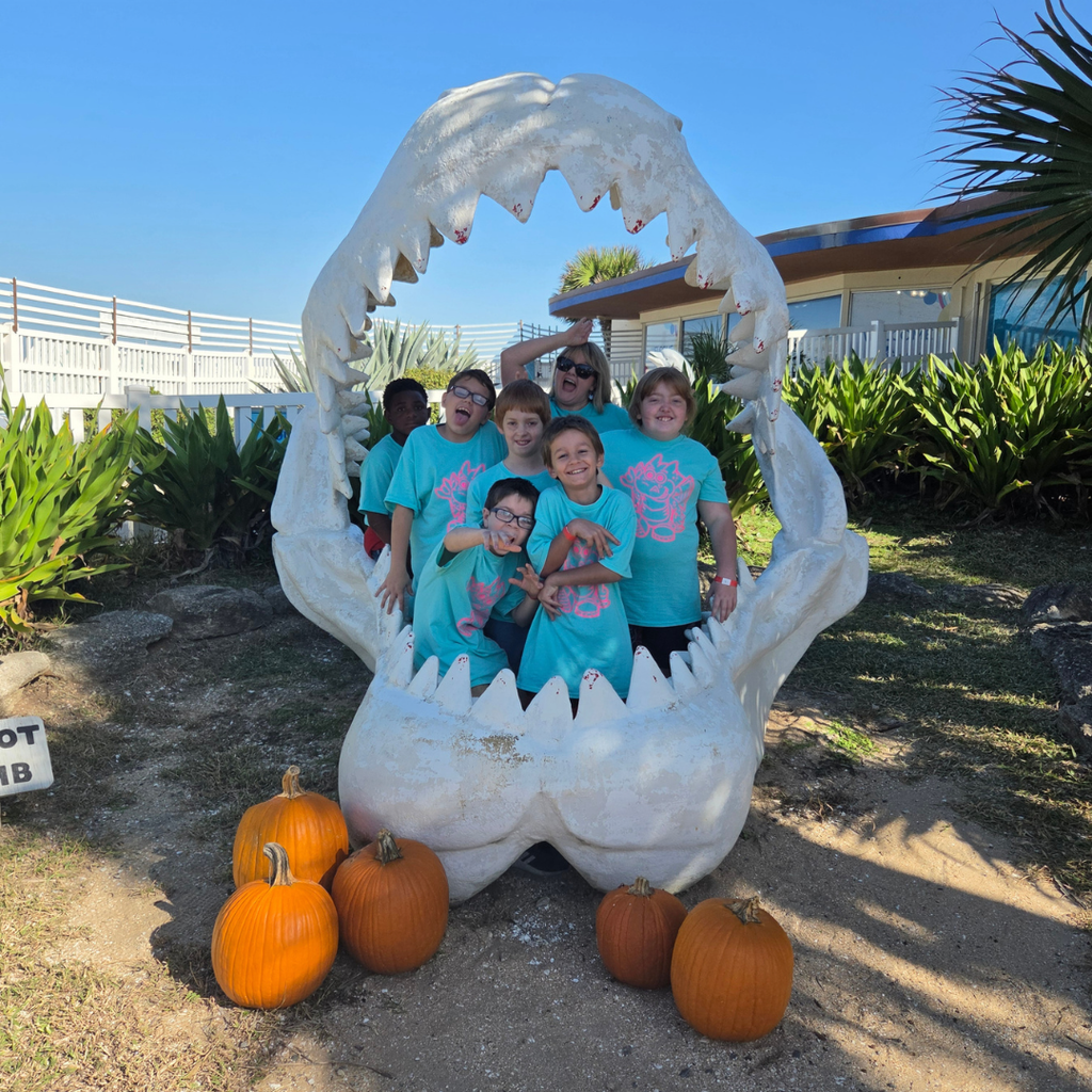 Group of students smile with their teacher inside a shark mouth statue.