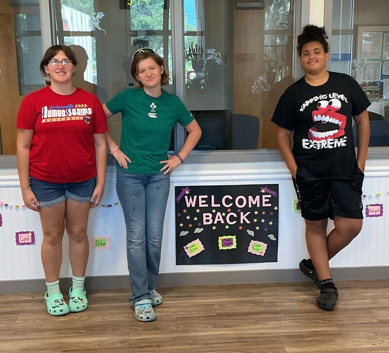 Three girls standing next to Welcome Back sign