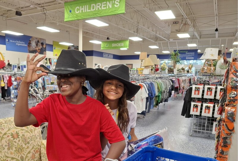 Two students wearing cowboy hats in a thrift store.