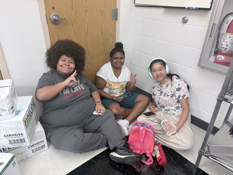 Three students sitting on the ground, giving peace signs to the camera.