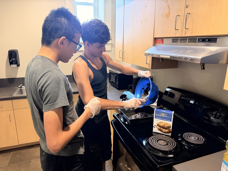 Two boys pouring a brownie mixture into a pan.