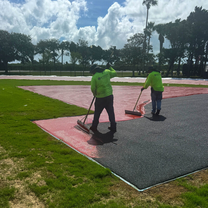 Two workers spreading red pain in the high jump area.