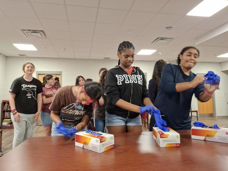 Girls practicing putting on blue latex gloves.