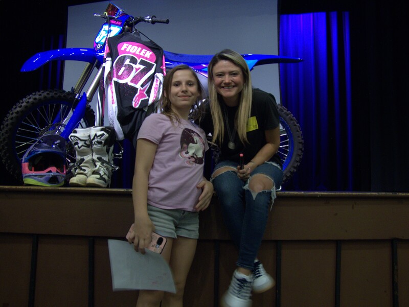 DMS student poses for a photo with Ashley Fiolek with her dirt bike on stage behind her.