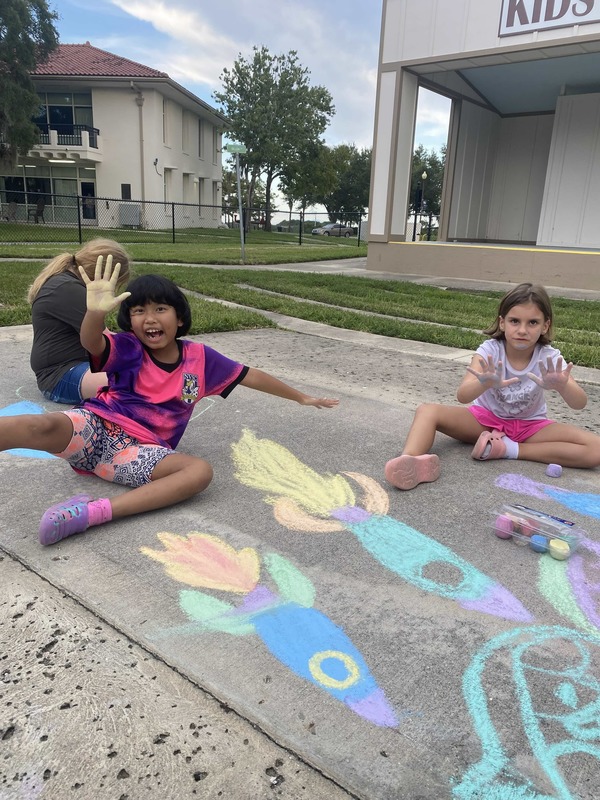 Girls drawing rockets with sidewalk chalk.