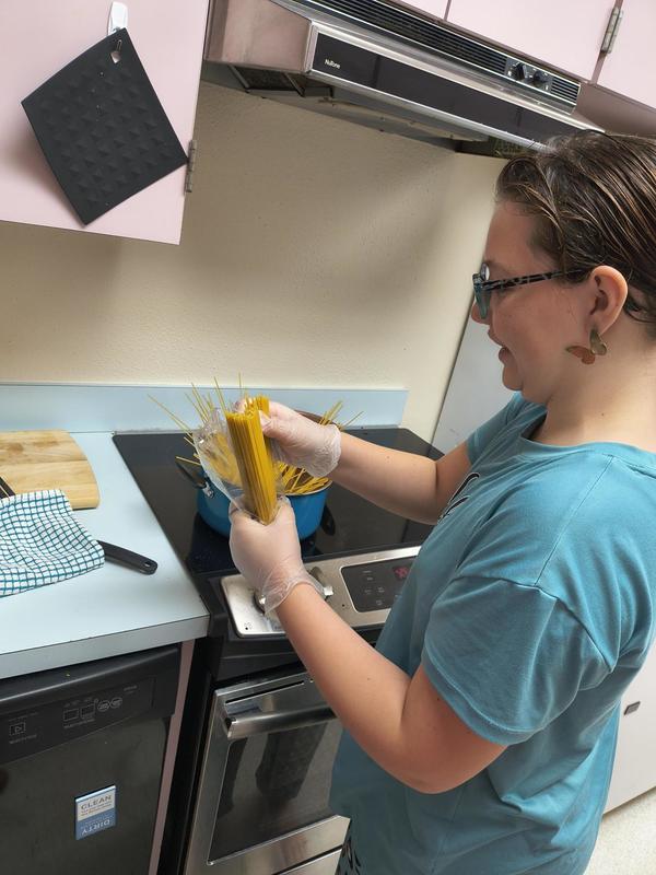 Girl putting pasta in a pan.