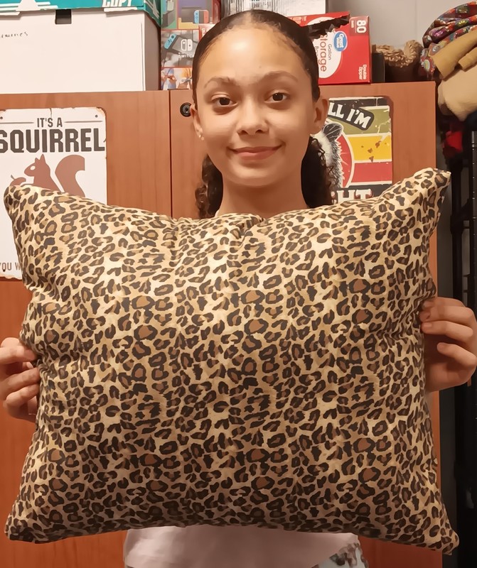 Girl holding an animal print pillow that she sewed together.