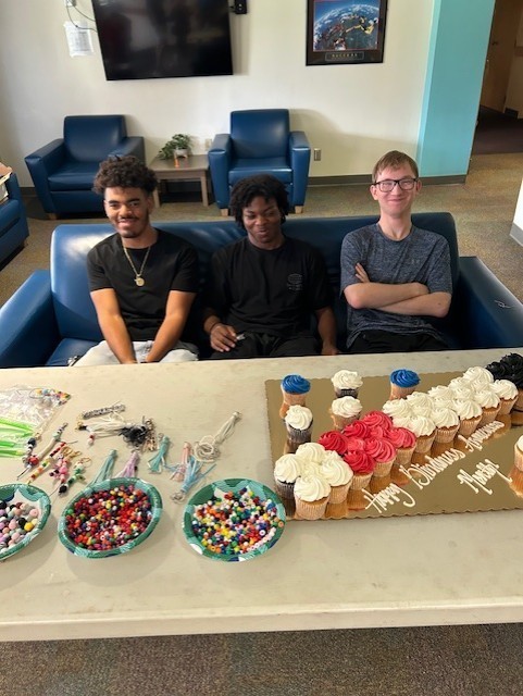 Three boys sitting on a couch behind the cupcakes