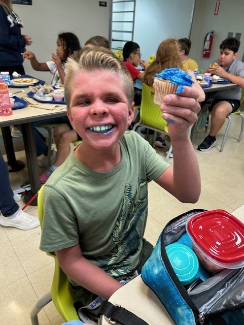 Boy smiling and holding a cupcake with blue icing.