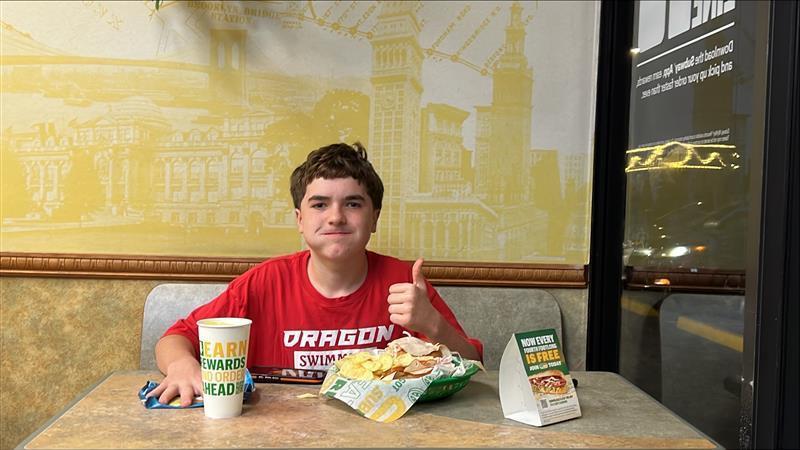 Student eating Subway in red Dragons shirt with thumbs up
