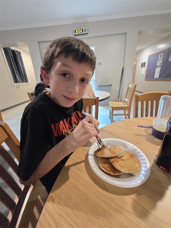 Student sitting down at table eating pancakes