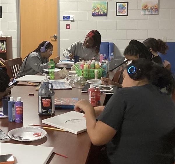 Girls sitting at table painting on canvas