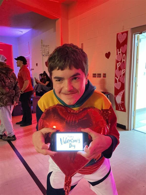 Student holding heart balloon and phone reading "Happy Valentine's Day" 