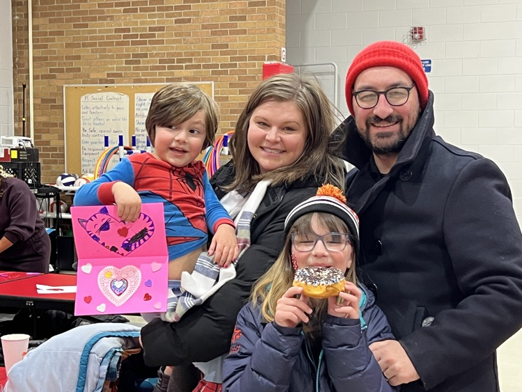 A family hugging each other, holding up a valentine and smiling